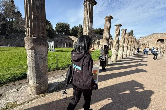 Visitors walking along a row of ancient columns in Pompeii