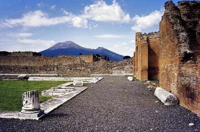 Un sentiero di ghiaia tra muri in rovina e colonne crollate a Pompei, con il Vesuvio alle spalle