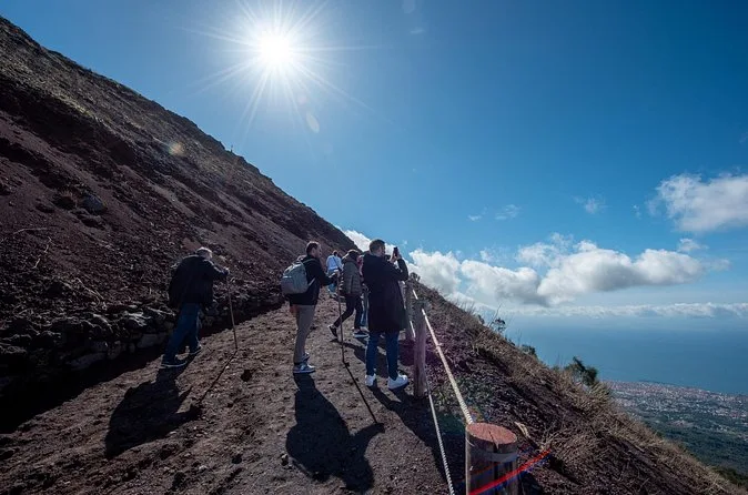 Wanderer steigen unter greller Sonne einen steilen Schotterweg am Vesuv hinauf