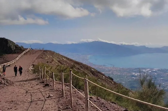 Wanderer auf dem eingezäunten Weg den Vesuv hinunter, unten die Bucht und die Küste